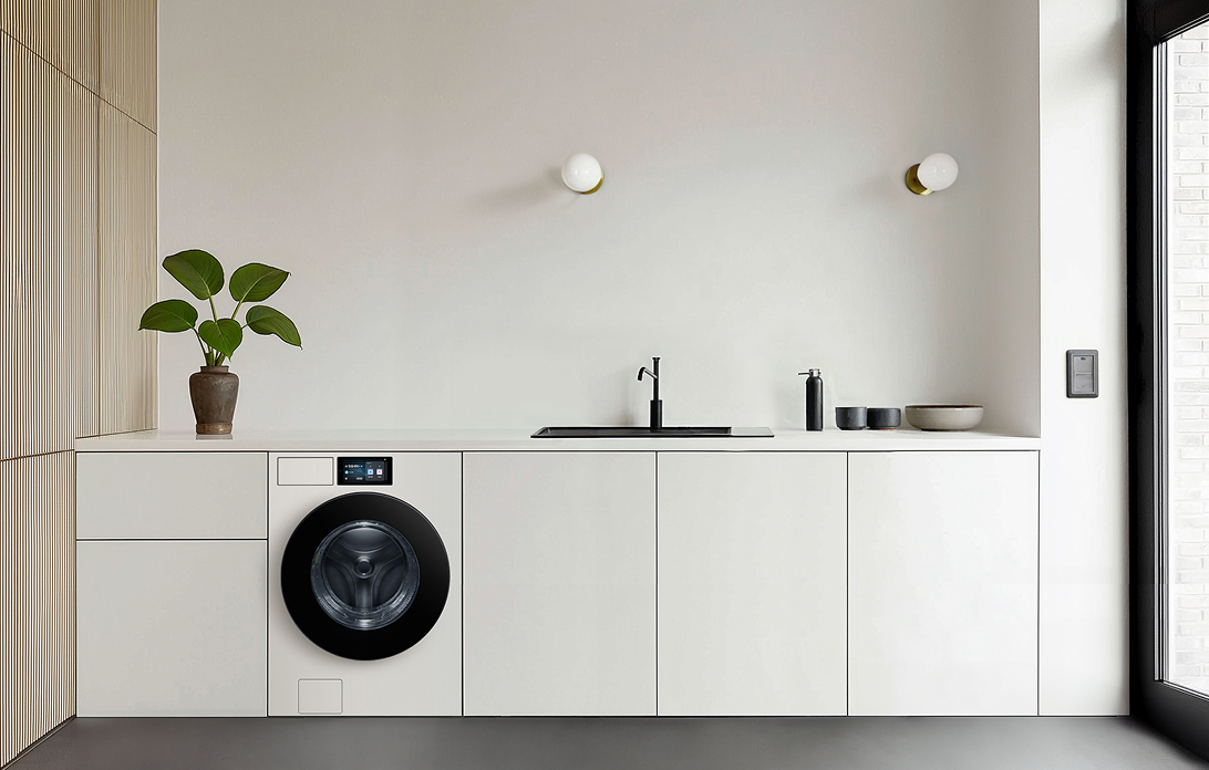 A front-load washer with a clean, built-in display is seamlessly integrated into a minimalist white kitchen interior.