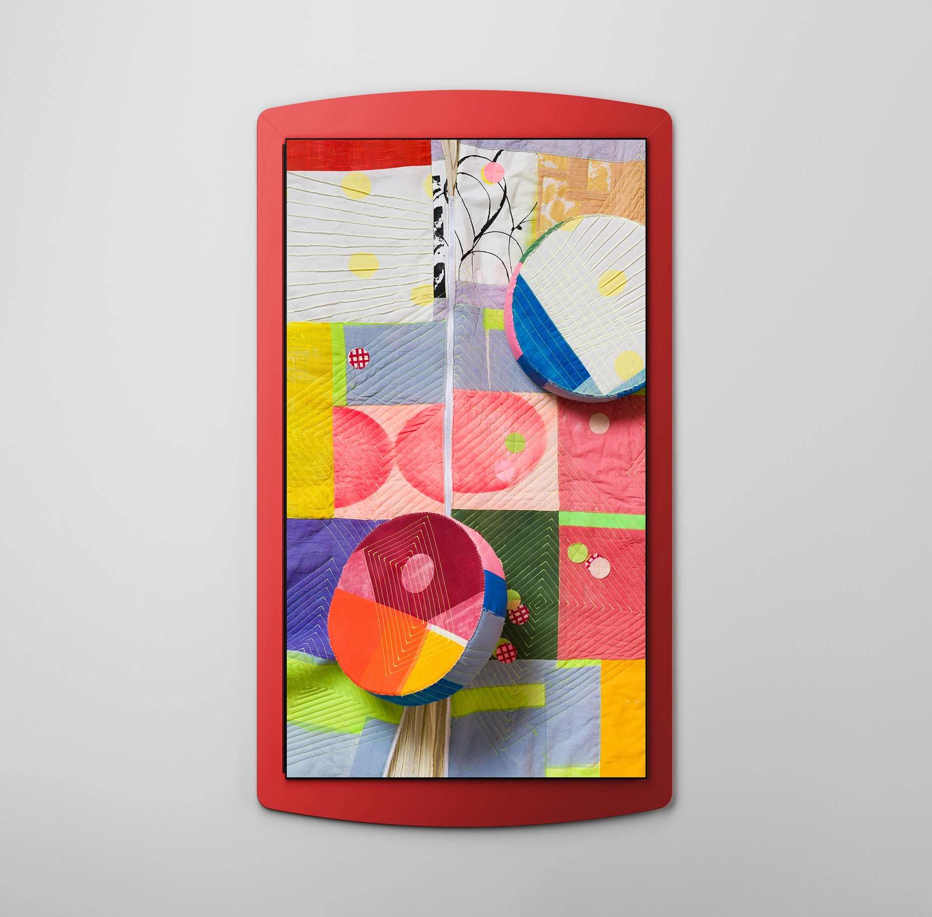 Inside a red metal frame with gently curved top and bottom edges is a quilt made of brightly colored stitched fabric pieces. Rounded fabric objects in multiple colors represent the Bespoke AI Steam Ultra, a low, round robot vacuum that moves across the floor.