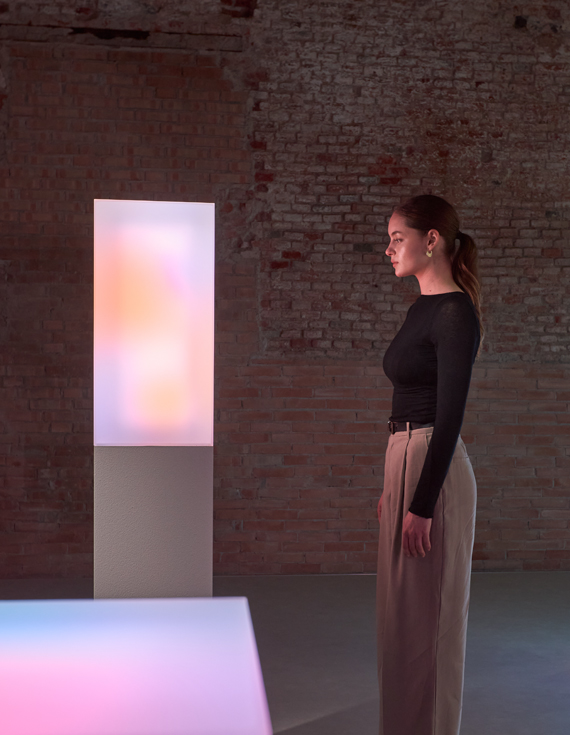 A white woman is looking at a glowing art installation that displays vibrant colors.