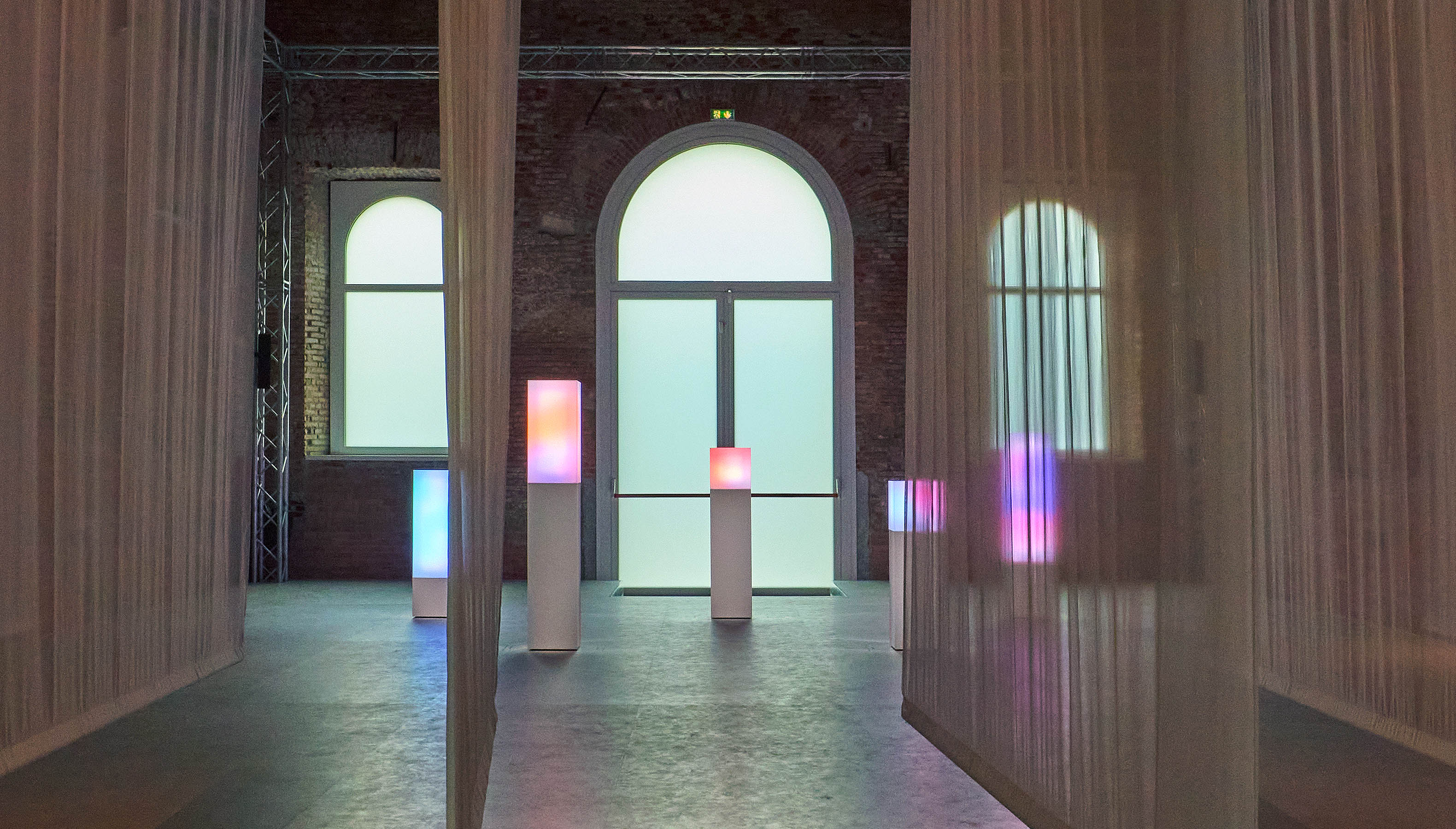 Transparent curtains create a hallway and the colorful light behind it is the image of a diameter inside a cube