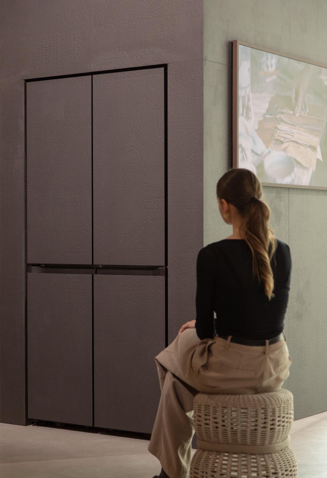 A white woman sits on a stool and observes a Bespoke sculpture in an understated color