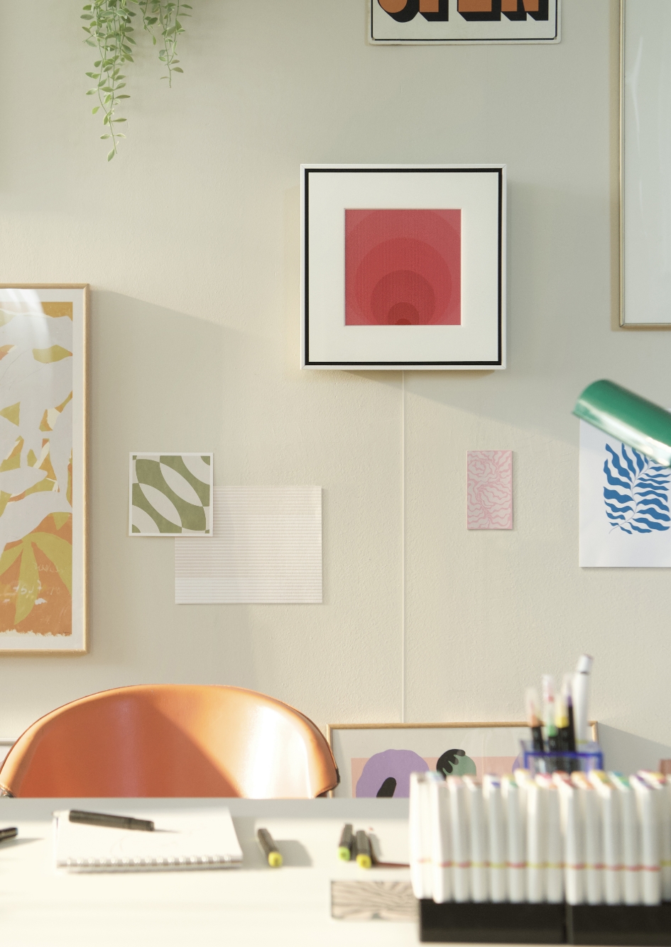 Daytime, bright sunlight illuminates a room that appears to be an artist's studio. A Music Frame hangs harmoniously on one wall alongside a variety of framed paintings. 