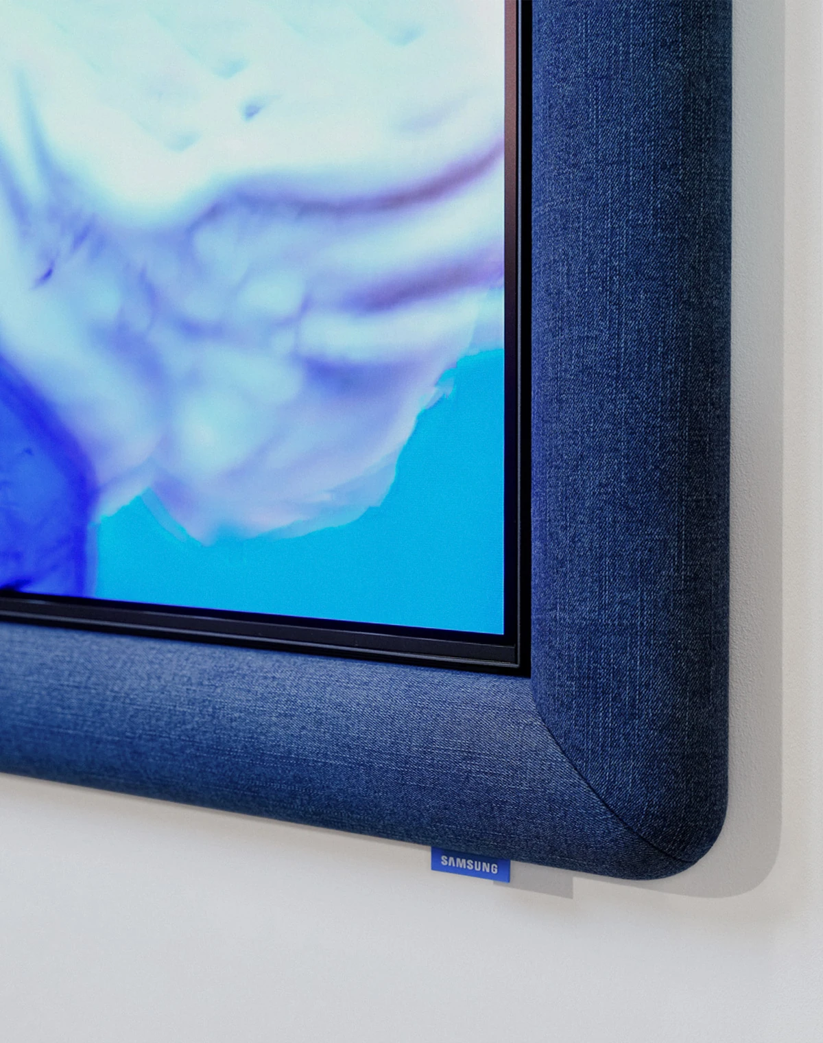Two white Galaxy Buds4 Pro wireless earbuds float inside a horizontal frame wrapped in dark blue fabric. They are surrounded by blue and white folded fabrics and soft, rounded forms.