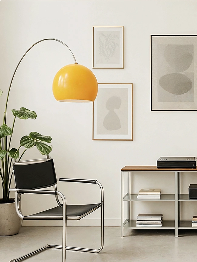 모던한 거실 인테리어 공간. 금속 프레임과 원목 상판의 선반 위에는 오디오 기기, 조명, 책, 화병 등이 놓여 있고, 왼쪽에는 블랙 가죽 의자와 화분이 배치되어 있다.